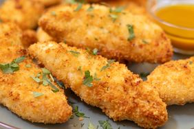 A plate of crispy chicken tenders garnished with herbs served with a side of dipping sauce