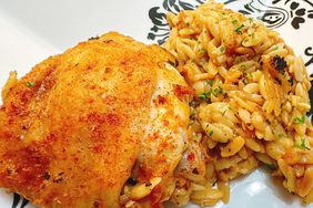 golden chicken thigh with herbed orzo on white plate