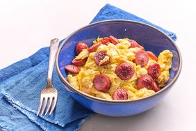 Scrambled Hot Dogs and Eggs in a blue bowl on a blue towel next to a fork 