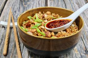 brown bowl of noodles topped with green onion and peanuts with spoonful of chili crisp