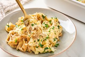 A serving of creamy tortellini garnished with herbs and a fork on a plate dish in background