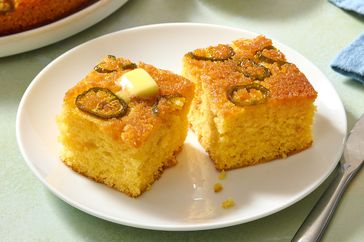 Two slices of jalapeo cornbread on a plate topped with a pat of butter with visible jalapeo slices