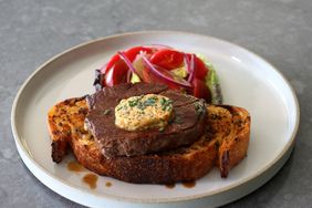 filet mignon steak with compound butter over toast on white plate with tomato salad