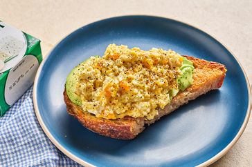 Scrambled eggs served on toast with avocado plated on a blue dish
