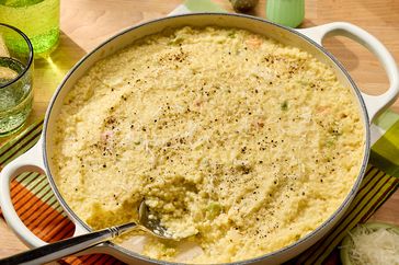 A dish of baked pasta casserole on a table with a spoon placed in it surrounded by tableware