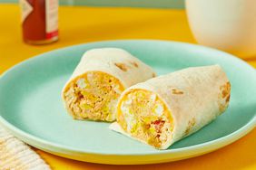 A breakfast burrito cut in half, served on a blue plate with coffee and hot sauce in the background