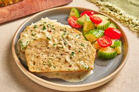 Two slices of meatloaf with sauce on a plate accompanied by sliced vegetables like zucchini and tomatoes