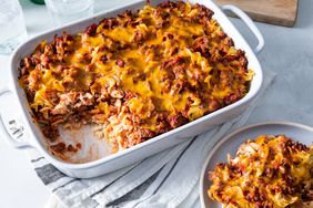 cheesy beef and pasta casserole in a white casserole dish with a portion taken out on a separate plate.
