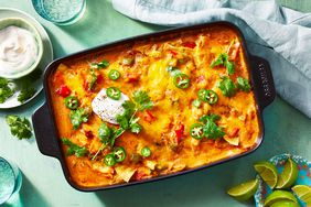 looking down at a casserole dish of king ranch chicken casserole, garnished with fresh herbs, pepper slices and sour cream, next to a plate with lime wedges