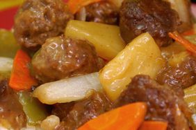 closeup of Sweet and Sour Meatballs with sliced carrots, bell peppers, onion, and pineapple chunks served over rice