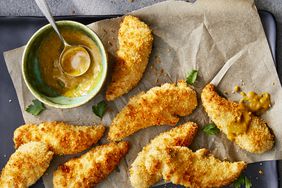 overhead view of Crumbed Chicken Tenderloins on a parchment paper lined baking sheet with herbs and sauce in a bowl