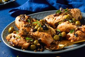 Chicken Marbella on an oval platter garnished with olives, plums, and fresh oregano