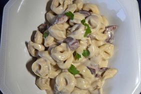 white platter with creamy tortellini and sausage