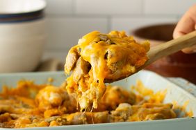 A cheesy eggplant casserole being served with a wooden spoon in a baking dish on a kitchen surface