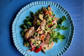 Blue ceramic fluted plate with chicken and vegetables and cream on blue placemat