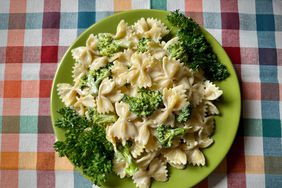 overhead view of green plate with bow-tie pasta with broccoli on bright checked tablecloth