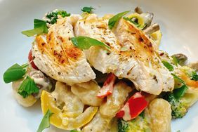 sauteed chicken breast cutlets on top of creamy gnocchi and vegetable mix on white plate