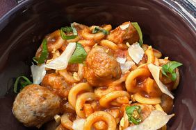 closeup of bowl of ring shaped pasta with tomato sauce, meatballs, basil, and Parmesan shavings