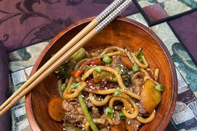 overhead view of chopsticks resting on wooden bowl of udon noodles with beef and vegetables