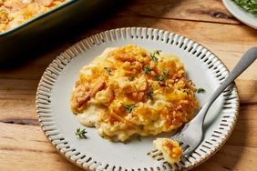 Million Dollar Potato Casserole garnished with thyme served on a plate with a fork, next to a baking dish 
