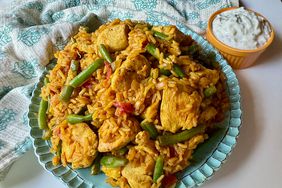 overhead view of turmeric chicken and rice with green beans and tomatoes on aqua plate with Indian print aqua towel and yellow ramekin of raita