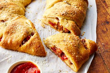 Sliced Pizza Stuffed Crescent Ring topped with grated cheese next to a bowl with red sauce 