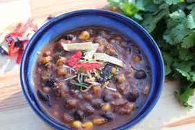 blue bowl of black bean beef tortilla soup on a board with cilantro and shredded cheese in background