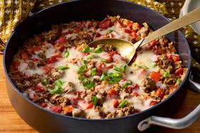 Cooked ground beef and rice skillet served with melted cheese and green onion, with a serving spoon 