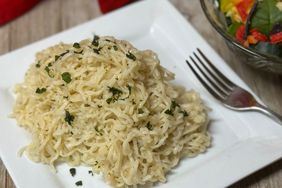 white plate of ramen with Parmesan and green salad in background