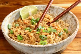 ceramic bowl of ramen with peanut butter sauce, green onions, lime wedge, chopsticks