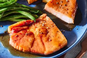 A plate with a sliced brown sugar ham steak, topped with cracked black better and served with green beans and potatoes