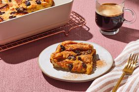 A plated portion of bread pudding, topped with cinnamon and served with coffee, with a baking dish of bread pudding in the background