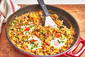 red skillet of mac and cheese with eggs and sausage on wooden table
