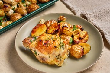 Roasted chicken with potatoes and herbs on a plate sheet pan meal visible in the background