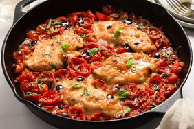 A skillet containing cooked chicken breasts with cherry tomatoes and garnish