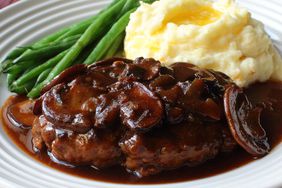 a plate of Chef John's Salisbury Steak topped with mushroom gravy, served with buttery mashed potatoes and green beans