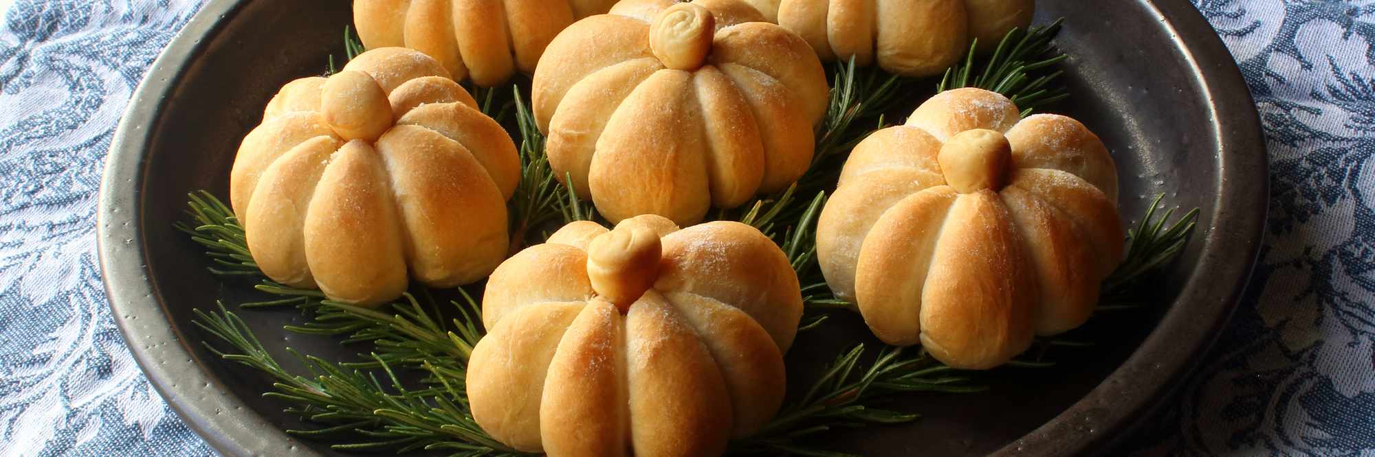 closeup of Pumpkin-Shaped Dinner Rolls on a serving plate garnished with rosemary sprigs