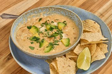 White chili topped with cilantro and avocado and tortilla chips on the side