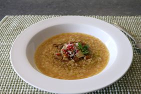 wide-rimmed white bowl of chicken soup with tiny star pastina on coarsely woven gray placemat