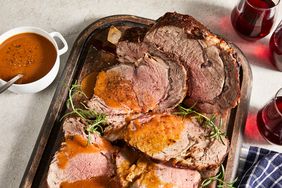 an overhead view of sliced rib roast on a cutting board dressed with jus and fresh rosemary