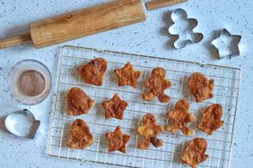 Pie crust cookies in the shape of stars and gingerbread man on wire rack with cookie cutters and rolling pin around