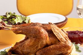 a straight on view of a golden brown turkey on a white oval platter dressed with fresh herbs and sliced lemons