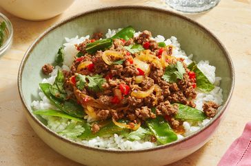A bowl of a stirfry dish served over rice including ground beef vegetables and garnished with herbs