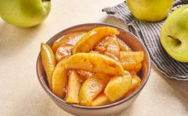 bowl of cinnamon fried apples with Golden Delicious apples and railroad stripe towel on pale counter