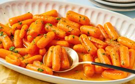 Dish of cooked baby carrots with a glaze and garnish served with a spoon