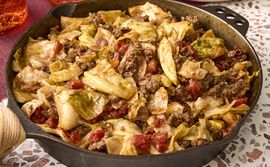 A skillet containing a dish with cooked cabbage ground meat and tomatoes resembling unstuffed cabbage rolls