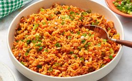 A bowl of Spanishstyle spiced rice garnished with chopped green onions and served with a spoon surrounded by a napkin and condiments