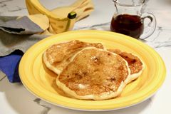 3 banana pancakes with maple syrup on yellow plate