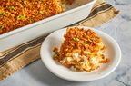 a low angle, close-up view of a heaping scoop of cheesy potato casserole plated in front of a casserole dish with remaining potato casserole.