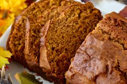 closeup of a loaf of Downeast Maine Pumpkin Bread, half cut into slices, on a white platter with fall leaf decor in the background
